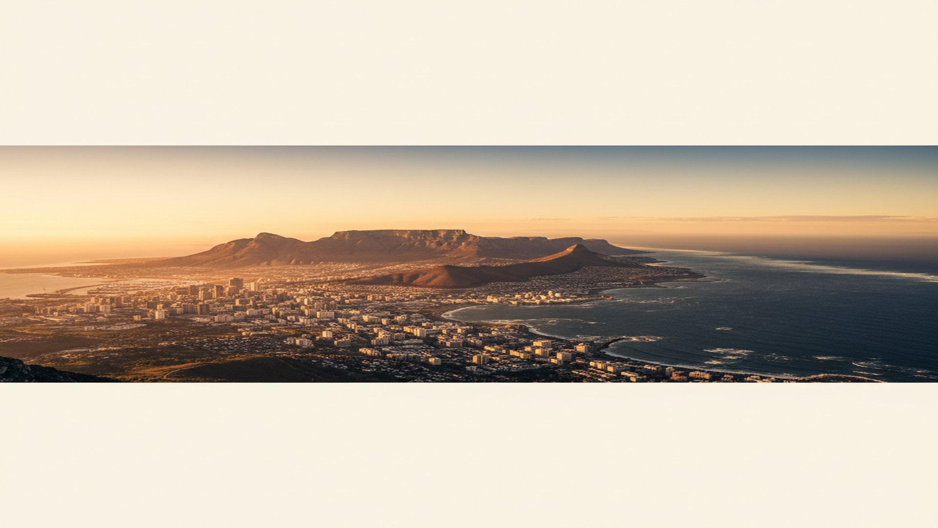 Cape Town skyline at golden hour — Table Mountain rising behind the city, the Atlantic seaboard glowing in late-afternoon light.