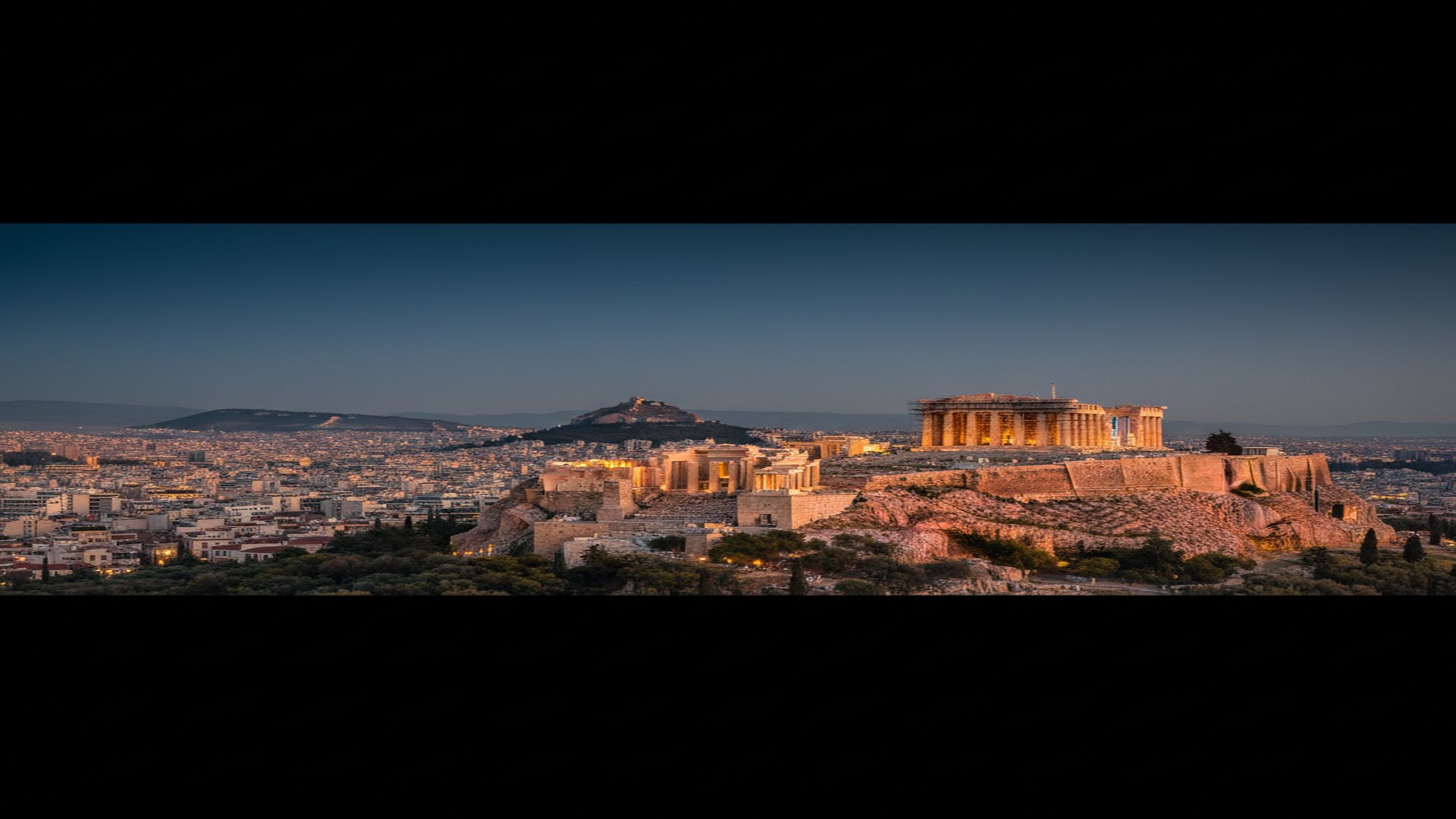 The Acropolis of Athens at golden hour with the Parthenon glowing against a deep-navy sky and the city of Athens stretching below.